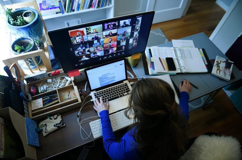 A teacher sits at home in front of a computer monitor.