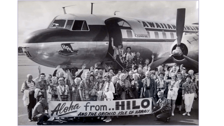 A group of people standing outside a plane holding a sign that says 'Aloha from Hilo'